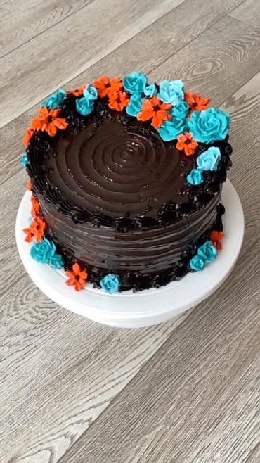 A dark chocolate cake with vibrant teal and orange flowers on one side.