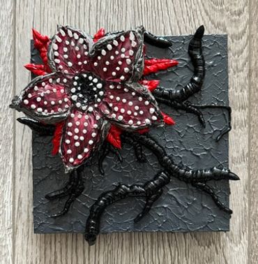 A dark, textured artwork featuring a red and black flower with white teeth and tentacle-like roots