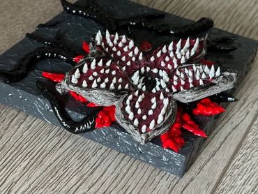 A dark, textured artwork featuring a red and black flower with white teeth and tentacle-like roots