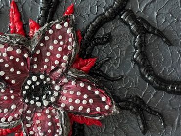 A dark, textured artwork featuring a red and black flower with white teeth and tentacle-like roots