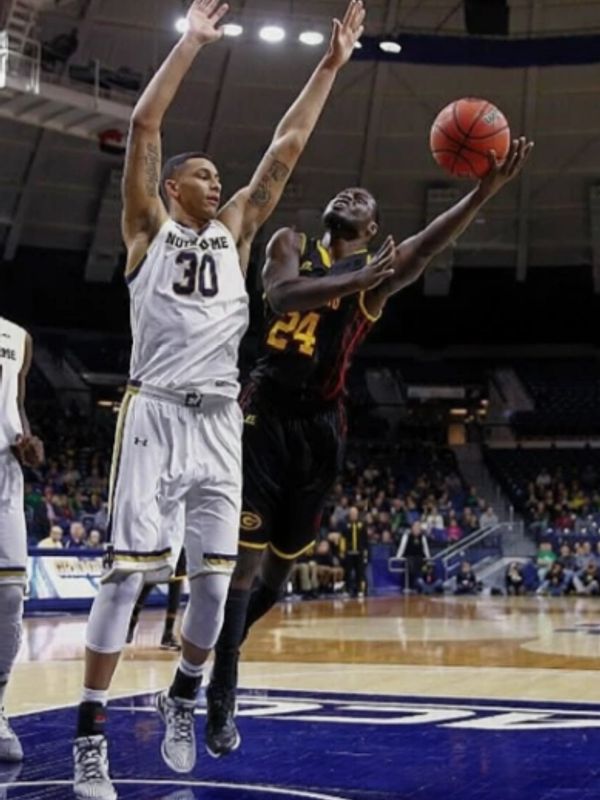 College basketball player attempts a layup while defender tries to block the shot.