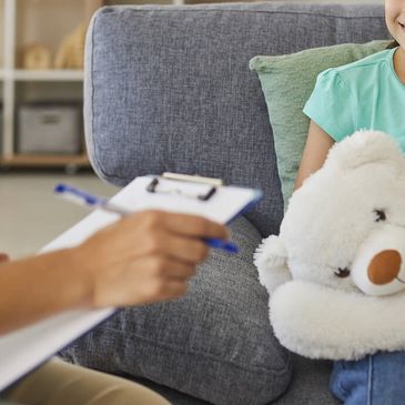 A young girl with a teddy bear during a therapy session.