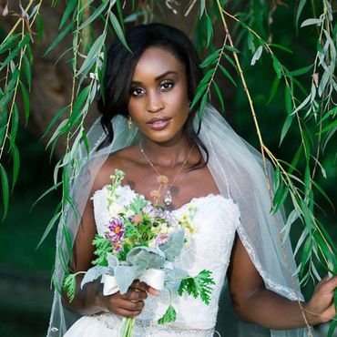 Bride in white dress holding a bouquet under green leaves.