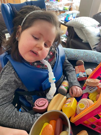 Child playing with toy food in a wheelchair.