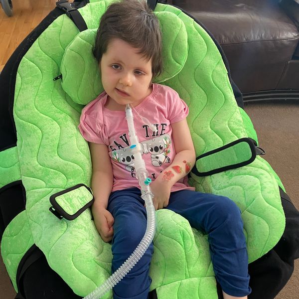 Child with medical equipment sitting in a green chair.