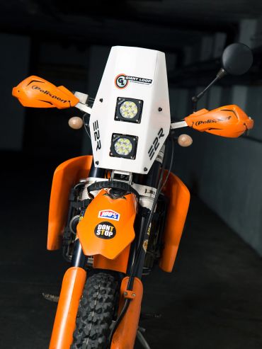 Moto naranja con protección en los espejos y faros delanteros cuadrados.