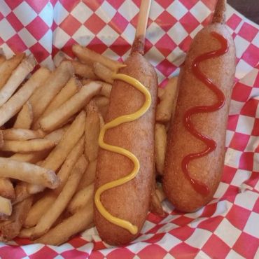 Two corn dogs with mustard and ketchup, served with fries.