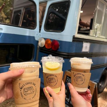 Drinks held up in front of blue school bus food truck