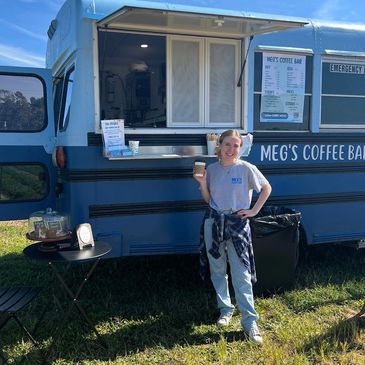 Owner standing in front of Megs coffee bar food truck in a field