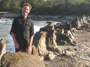 Psychic Jethro in Hawaii standing by the water on a beach with pointed rocks