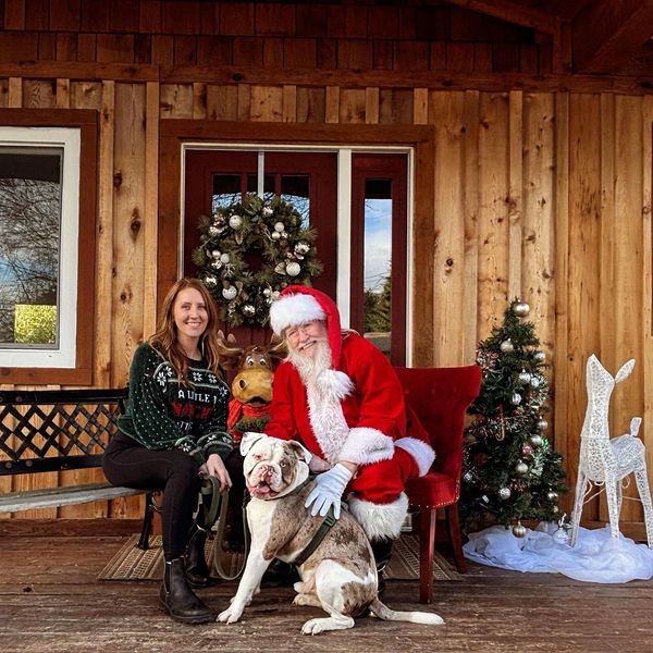 Woman and Santa with a dog on a decorated porch.