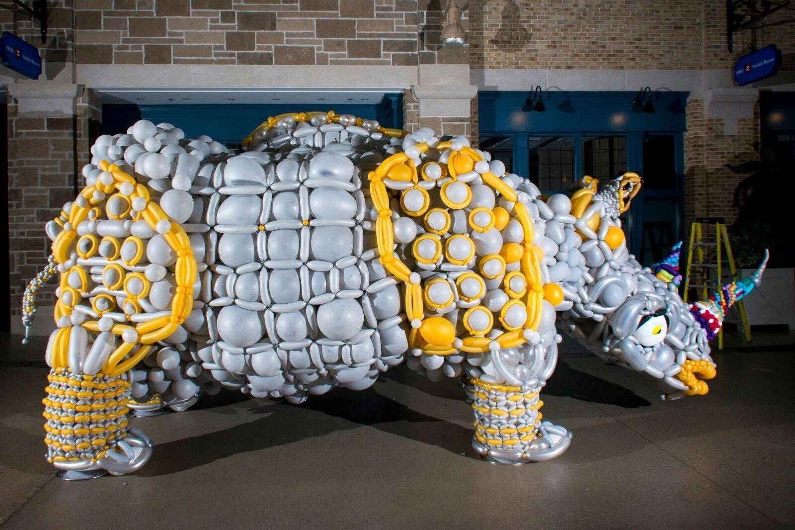 A large rhinoceros sculpture made entirely of balloons in silver and yellow.