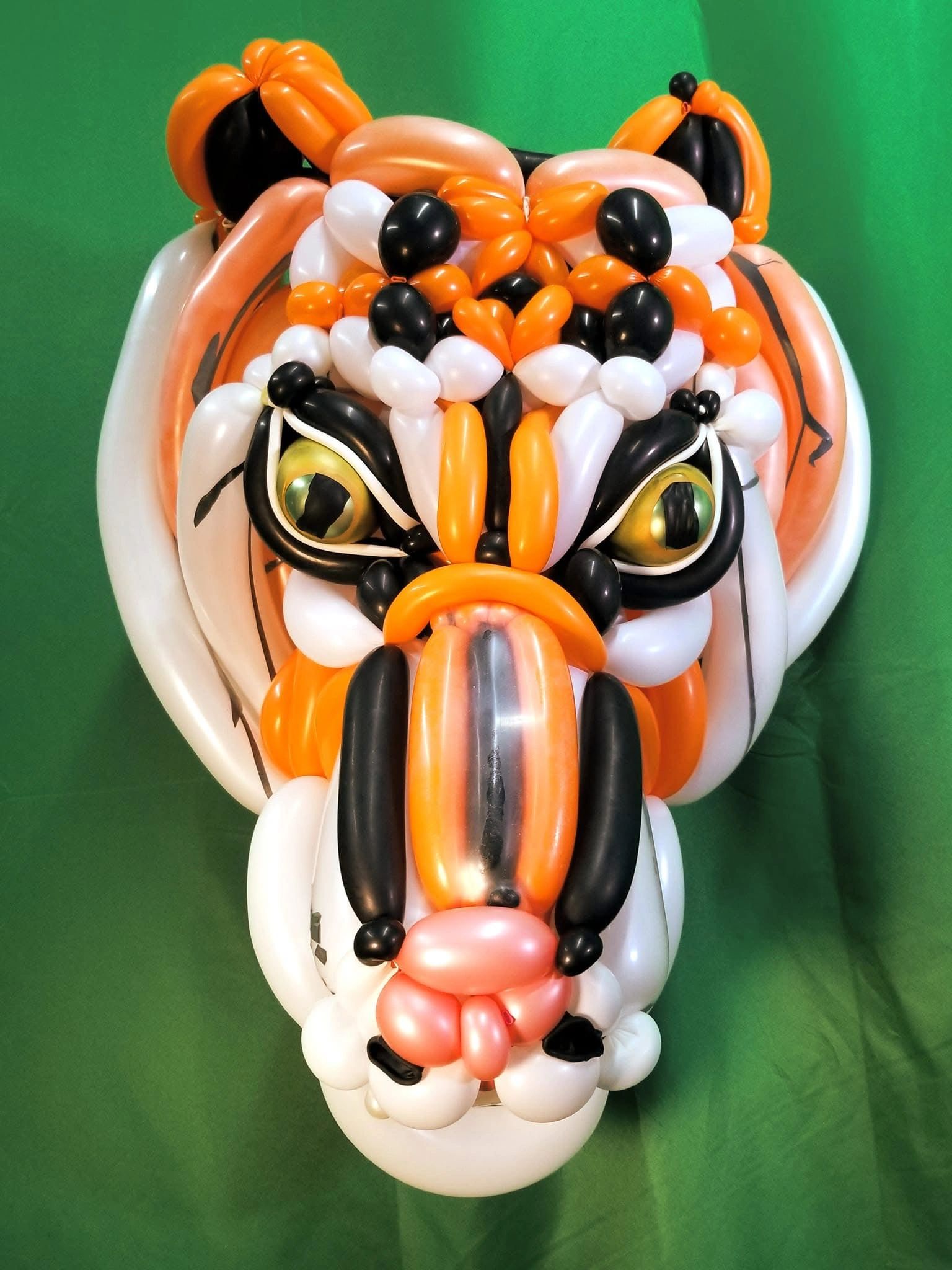 A detailed tiger face sculpture made from orange, white, black, and pink balloons.