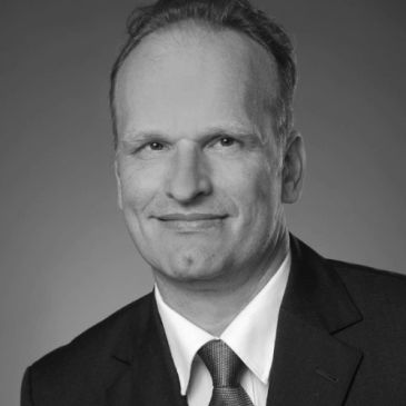 Professional black and white headshot of a man in a suit and tie.