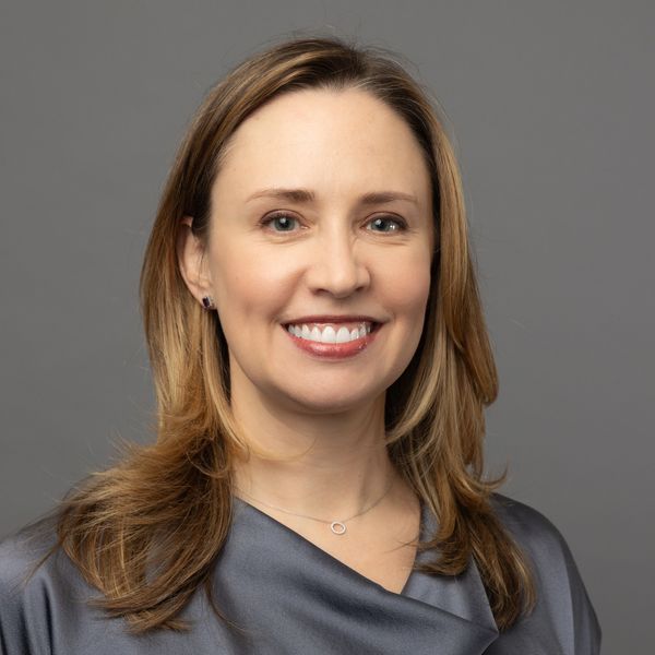 Professional woman with light brown hair smiling against a gray background.