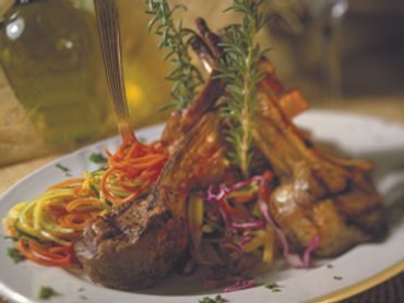 Grilled lamb chops with colorful vegetable noodles and fresh rosemary garnish.