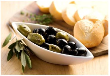 Bowl of seasoned green and black olives with fresh bread rolls.
