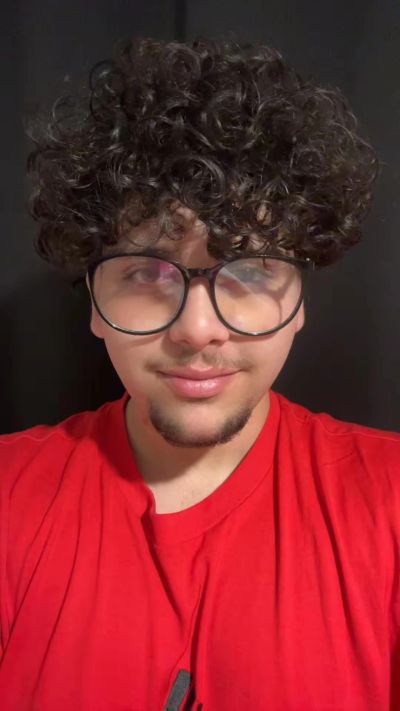 Young man with curly hair and glasses in a red shirt.
