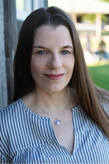 A woman with long brown hair smiling gently outdoors.