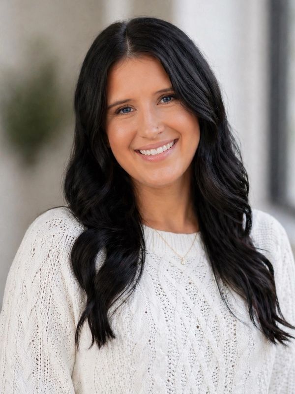 Smiling woman with dark wavy hair wearing a white knit sweater.