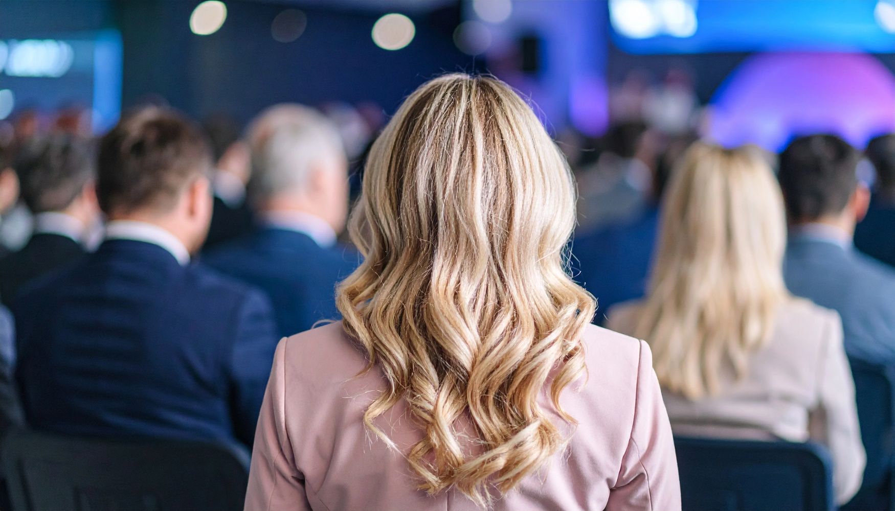 Blonde woman attending a formal event with others in business attire.