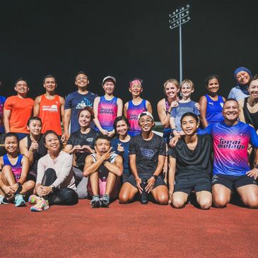 A diverse group of runners posing together on a track at night.