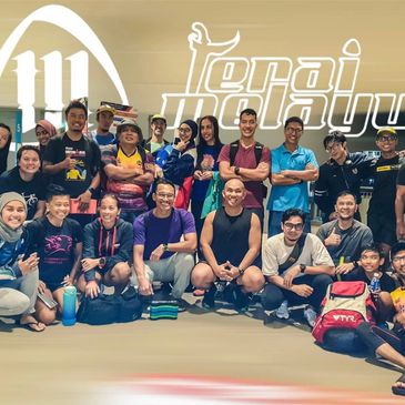 A diverse group of people posing together in a gym setting with a sports logo background.