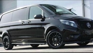 Sleek black Mercedes-Benz van parked outside a modern building.