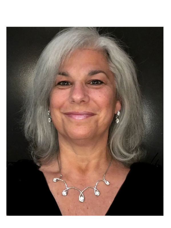 Jackie Shepard- Smiling woman with silver hair wearing elegant jewelry and a black top.