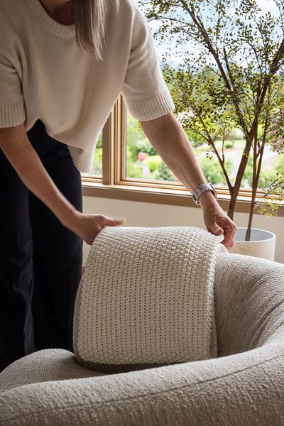 Hands styling a cream textured pillow in a warm, light-filled living space
