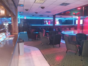 Empty lounge with a neon-lit stage and cozy chairs.