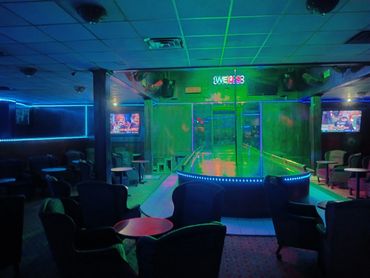 Dimly lit lounge with neon lights and a central stage with a pole.