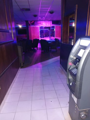 Dimly lit lounge with neon lights, chairs, and an ATM machine near the entrance.