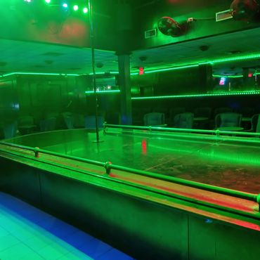 Empty nightclub stage with a pole under green lighting.