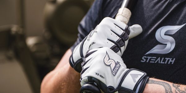 Close-up of a man holding a baseball bat wearing Stealth gloves and a black shirt.
