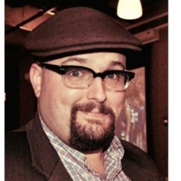 Man with glasses and hat smiling.