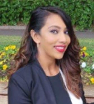 Woman smiling outdoors with flowers in background.