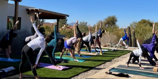 Group practicing outdoor yoga with raised arms on mats under clear blue sky.