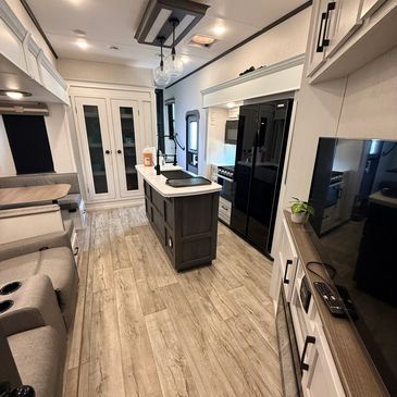 Modern, compact RV kitchen and dining area with wood flooring.