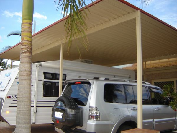Silver SUV parked under a carport beside a white trailer in a tropical setting.