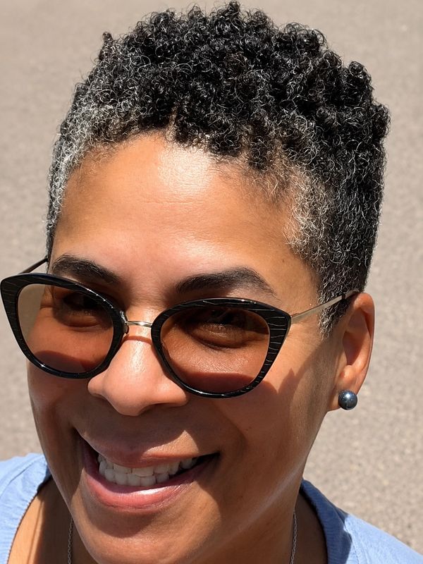 Smiling person wearing sunglasses with curly hair.
