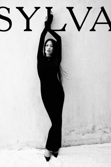 Woman in a long black dress posing against a textured wall with 'SYLVA' text.