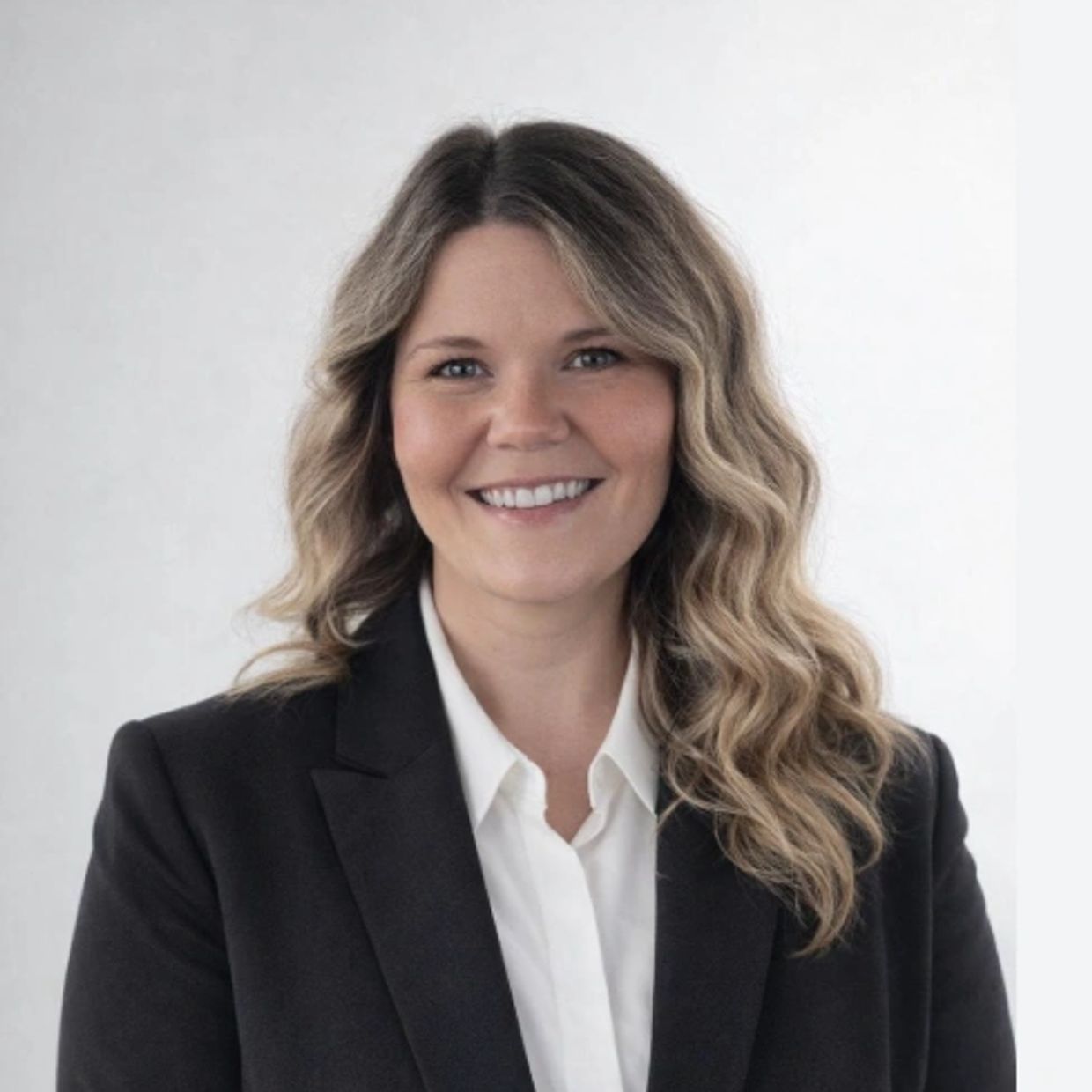 Professional woman with wavy hair wearing a black blazer and white shirt.