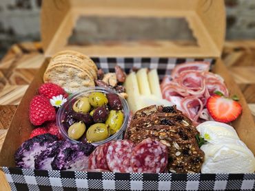 A gourmet charcuterie box with meats, cheeses, olives, fruits, nuts, and crackers.