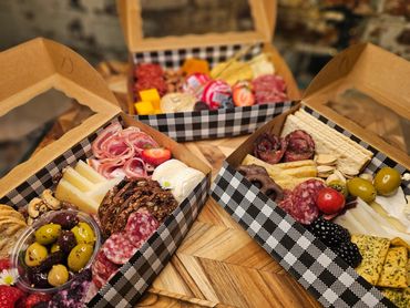 Three gourmet charcuterie boxes with meats, cheeses, olives, and fruits.