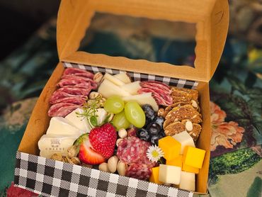 A colorful charcuterie box with cheese, meats, fruits, nuts, and crackers.