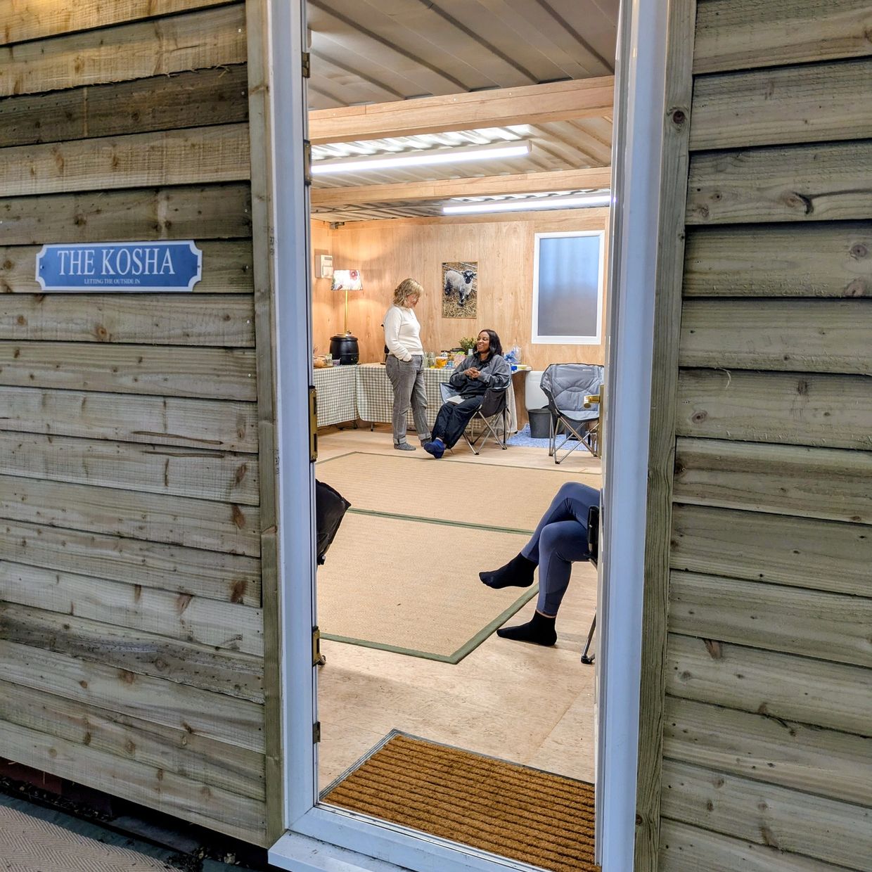People relaxing and chatting inside a wooden cabin named 'The Kosha'.