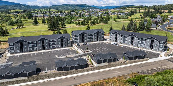 Aerial view of a modern apartment complex with parking and green hills.