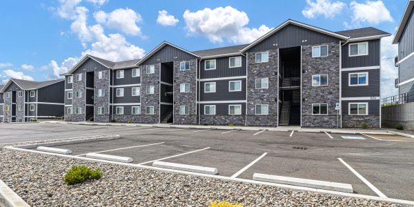 Modern three-story apartment complex with empty parking and a clear blue sky.