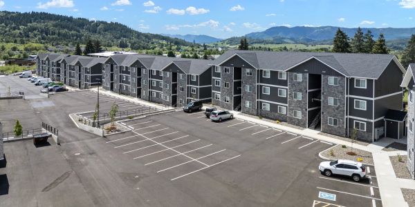 Newly constructed apartment complex with ample parking and mountainous backdrop.